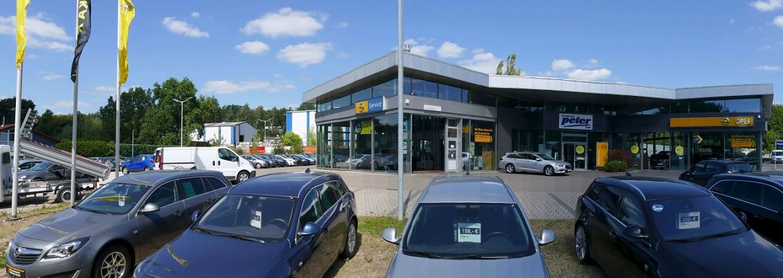Opel Autohaus Peter in Osterode mit moderner Glasfassade, mehreren Opel-Fahrzeugen auf dem Parkplatz und gelben Opel-Fahnen im Vordergrund.