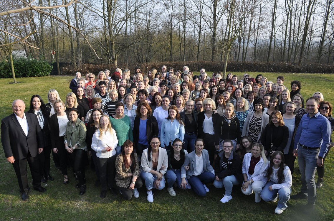 Gro&szlig;es Gruppenfoto im Freien bei der Frauentagsfeier der Autohaus Peter Gruppe. Zahlreiche Frauen und einige M&auml;nner stehen dicht beieinander auf einer Wiese, im Hintergrund kahle B&auml;ume an einem sonnigen Tag.