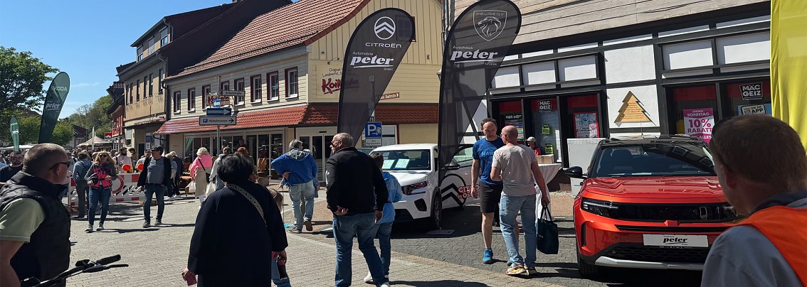 Belebte Bad Lauterberger Innenstadt bei Sonnenschein mit Besuchern und Autos der Marken Citro&euml;n, Peugeot und Opel vor Ausstellungszelten.