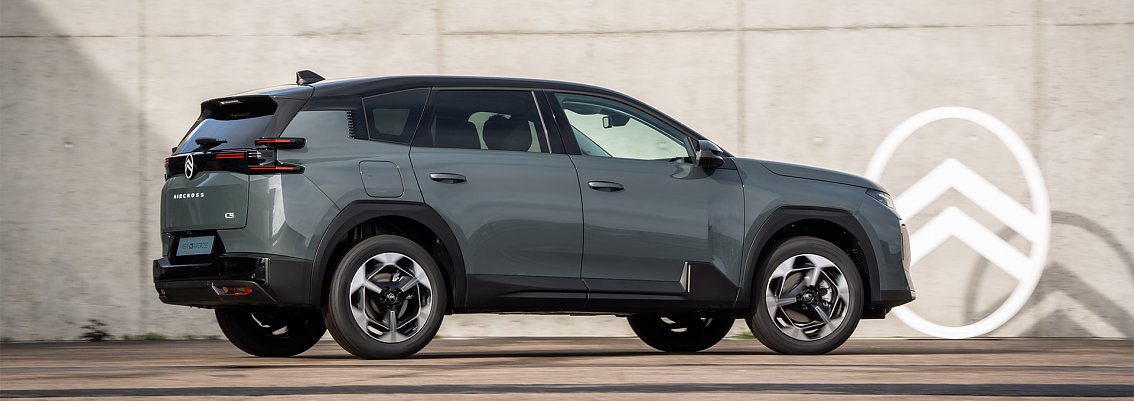 Seitenansicht des neuen Citro&euml;n C5 Aircross in Grau, fahrend vor einer Betonwand mit Citro&euml;n-Logo.