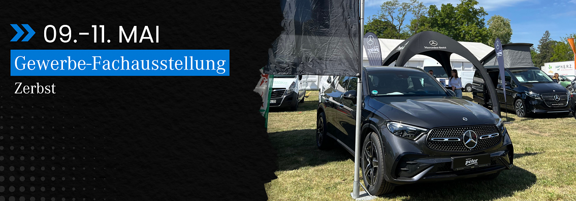 Veranstaltungsbanner und Fahrzeugpr&auml;sentation: Schwarzes Banner mit Text 09.�11. Mai, Gewerbe-Fachausstellung Zerbst neben einem ausgestellten grauen Mercedes-Benz SUV vor dem Stand der Autohaus Peter Gruppe.