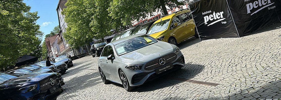Mercedes-Benz Ausstellung bei der NOM MOT 2025: Mehrere Mercedes-Benz Fahrzeuge, darunter ein silberner Kompaktwagen im Vordergrund, sind in einer Reihe auf einem gepflasterten Platz ausgestellt, flankiert von Bannern der Autohaus Peter Gruppe.