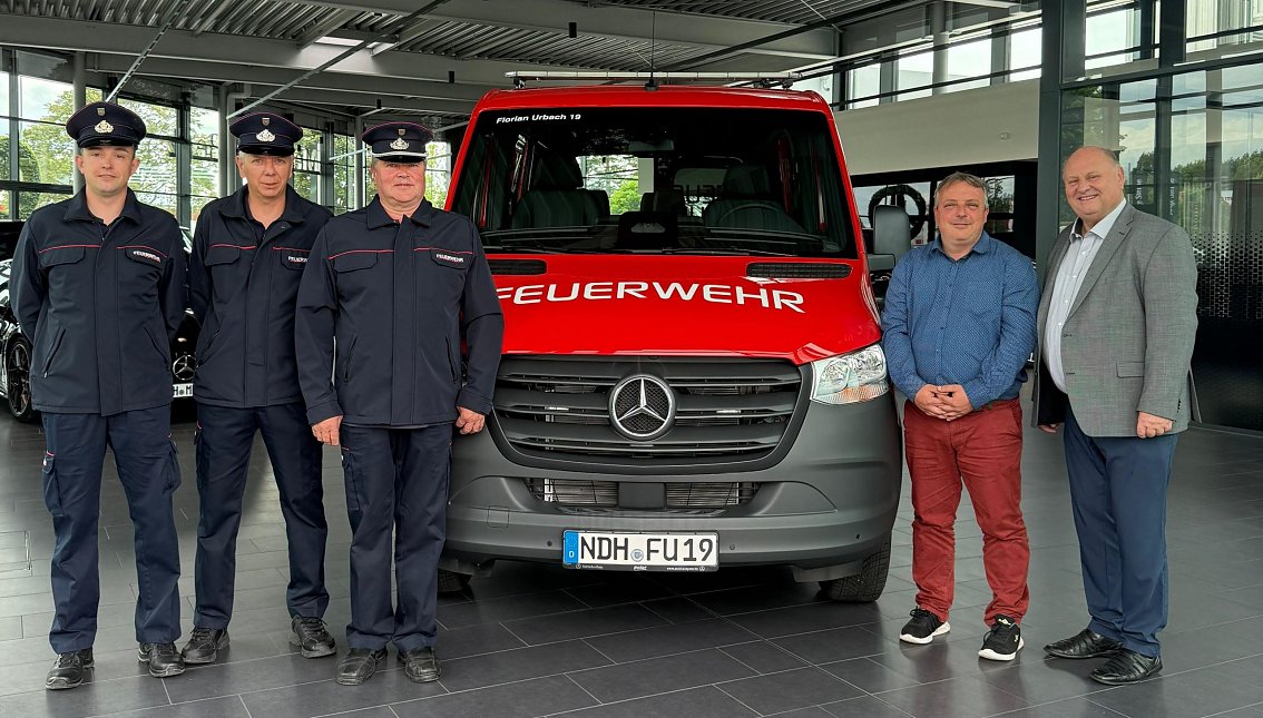 &Uuml;bergabe eines neuen Mannschaftstransportwagens an die Freiwillige Feuerwehr Urbach durch das Autohaus Peter. Vor dem roten Feuerwehrfahrzeug mit der Aufschrift �FEUERWEHR� stehen drei Feuerwehrm&auml;nner in Uniform sowie Ortsb&uuml;rgermeister Markus Volkmann und unser Gesch&auml;ftsf&uuml;hrer Helmut Peter. Das Foto wurde im Ausstellungsraum des Autohauses aufgenommen.
