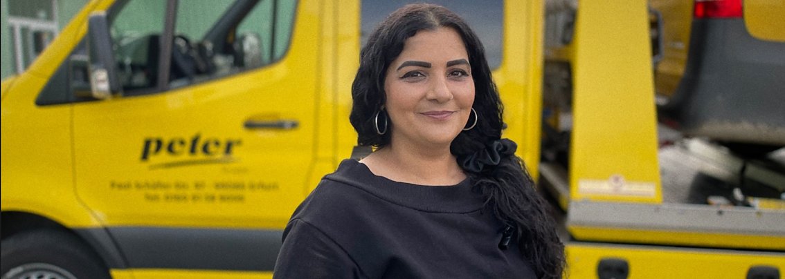 Eine Frau mit langen dunklen Haaren lächelt in die Kamera. Sie steht vor einem gelben ADAC Fahrzeug.