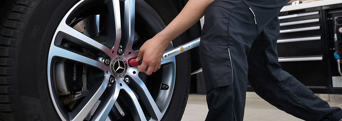 Ein Mitarbeiter zieht mit einem Drehmomentschl&uuml;ssel die Radschrauben an einer Fahrzeugfelge von einem Mercedes-Fahrzeug fest.