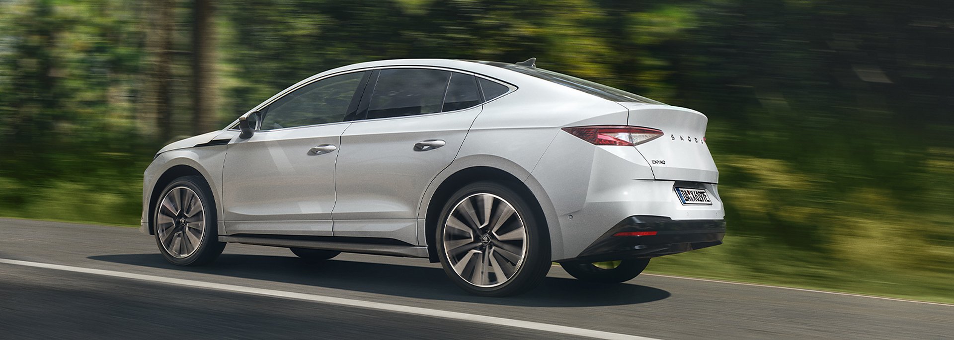 Skoda Enyaq Coup&eacute; in wei&szlig; f&auml;hrt schnell auf einer Stra&szlig;e im Wald