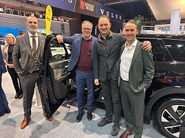 Vier Männer (u.a. Mario Voigt und Andreas Peter) stehen lächelnd neben einem schwarzen Auto mit geöffneter Tür. Im Hintergrund sind die Logos von Opel, Volvo und Renault Trucks auf Bannern zu erkennen.