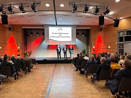 Auf einer großen Leinwand steht Die Automobilmesse Erfurt 2025 ist eröffnet!. Davor sprechen drei Männer (rechts Helmut Peter) auf einer Bühne, während zahlreiche Besucher im Saal zuhören.