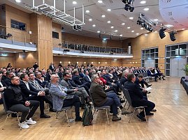 Weitwinkelaufnahme des Saals mit vielen Gästen, die aufmerksam nach vorn zur Bühne schauen.