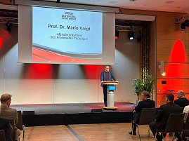 Prof. Dr. Mario Voigt spricht am Rednerpult der Messe Erfurt, im Hintergrund eine Leinwand mit seinem Namen und Titel als Ministerpräsident Thüringens.