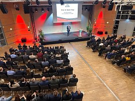 Blick von oben auf die Bühne: Prof. Dr. Mario Voigt hält eine Rede, sein Name steht groß auf der Leinwand.