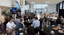 Torsten Wiesner h&auml;lt einen Vortrag mit der Pr&auml;sentation Herausforderungen der Energiewende. Teilnehmende sitzen an runden Tischen mit Kaffee und Fr&uuml;hst&uuml;cksplatten.