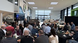 Ein Referent h&auml;lt einen Vortrag mit der Pr&auml;sentation Herausforderungen der Energiewende. Teilnehmende sitzen an runden Tischen mit Kaffee und Fr&uuml;hst&uuml;cksplatten.