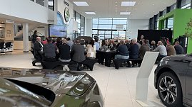 R&uuml;ckansicht der G&auml;ste, die an Fr&uuml;hst&uuml;ckstischen sitzen und einer Pr&auml;sentation zuh&ouml;ren. Links im Bild die Rednerin, rechts der gro&szlig;e �koda-Schriftzug an der Wand.