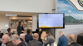Eine Rednerin zeigt auf eine Folie mit Diagrammen und dem Titel Herausforderungen. Im Vordergrund sitzen Teilnehmende, die zuh&ouml;ren.