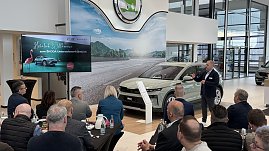 Ein Referent spricht vor einem Publikum, w&auml;hrend der neue �koda Elroq im Showroom pr&auml;sentiert wird. Links auf einem Bildschirm die Begr&uuml;&szlig;ungsfolie Herzlich Willkommen zum �KODA Unternehmerfr&uuml;hst&uuml;ck.