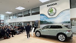 Der neu vorgestellte �koda Elroq steht in voller Gr&ouml;&szlig;e im Ausstellungsraum. Im Hintergrund sitzen G&auml;ste und h&ouml;ren dem Vortragenden zu. &Uuml;ber dem Auto h&auml;ngt das gro&szlig;e �koda-Logo.