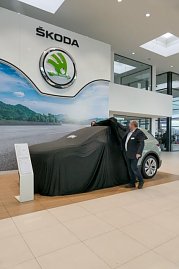 Ein �koda Elroq ist noch mit einem schwarzen Tuch abgedeckt. Ein Mitarbeiter zieht die Abdeckung teilweise zur Seite. Das gro&szlig;e �koda-Logo h&auml;ngt an der Wand.