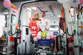 Ein ge&ouml;ffneter Rettungswagen steht im Autohaus. Zwei Mitarbeitende des Deutschen Roten Kreuzes stehen darin, vor ihnen sitzt ein gro&szlig;es Stoff-Einhorn auf einer Krankentrage. Rosa Luftballons schm&uuml;cken den Wagen.