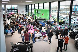 Blick von oben in den hellen Ausstellungsraum des Autohauses. Viele Besucher schauen sich an langen Tischen bunte Schulranzen an. Im Hintergrund stehen Autos, rosa Flamingos als Deko h&auml;ngen von der Decke.
