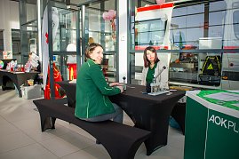 Zwei Frauen sitzen an einem schwarzen Tisch mit Infomaterial. Im Hintergrund steht ein Rettungswagen. Auf dem Tisch liegen Ger&auml;te, vermutlich f&uuml;r eine Mitmachaktion. Rechts ist ein gr&uuml;ner Stand der AOK Plus zu sehen.