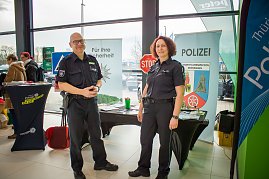 Zwei Polizisten in Uniform stehen vor einem Infostand der Landespolizeiinspektion Nordhausen. Hinter ihnen Banner mit Polizeiwappen, Infomaterial und einem Stoppschild.
