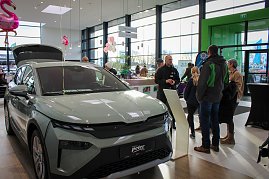 Ein neues �koda-Fahrzeug mit ge&ouml;ffnetem Kofferraum steht im hellen Showroom. Besucher unterhalten sich daneben, rosa Flamingo-Dekorationen h&auml;ngen von der Decke.