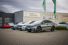 Mehrere �koda-Fahrzeuge stehen vor dem Geb&auml;ude �koda Plus Autowelt Peter. Zwei gr&uuml;ne Fahnen wehen im Vordergrund. Links im Bild parken weitere Autos.