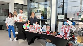 Vier Personen stehen hinter einem Infostand im �koda Autohaus. Auf dem Tisch liegen Brosch&uuml;ren und ein Gl&uuml;cksrad. Die Personen tragen Kleidung mit Logos des Deutschen Roten Kreuzes.