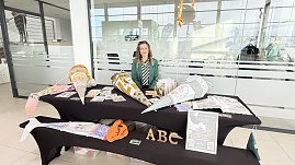 Eine Frau sitzt hinter einem Stand im Autohaus. Auf den Tischen liegen farbenfrohe, gro&szlig;e Schult&uuml;ten und Informationsmaterialien. Vorne gro&szlig;e Buchstaben ABC.