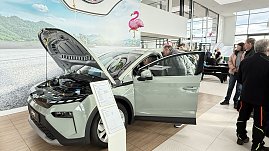 Ein helles �koda-Fahrzeug mit ge&ouml;ffneter Motorhaube und Fahrert&uuml;r steht im Showroom. Besucher betrachten das Auto, im Hintergrund Flamingo-Dekoration.