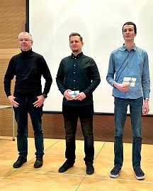 Robert Rausch und Florian Kahl stehen neben ihrem Berufsschullehrer. Beide halten einen Geschenkgutschein, w&auml;hrend sie f&uuml;r die Auszeichnung posieren.