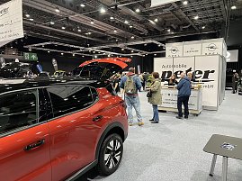 Besucher stehen vor dem Info-Counter von Autohaus Peter. Daneben ein rotes Opel-Fahrzeug mit ge&ouml;ffnetem Kofferraum.