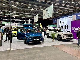 Ein blauer Peugeot und ein wei&szlig;er Peugeot SUV nebeneinander auf der Ausstellungsfl&auml;che, im Hintergrund gro&szlig;e Messebanner und lilafarbene Wand So l&auml;uft Laden.