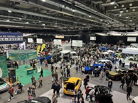 Breiter &Uuml;berblick &uuml;ber die Automobilmesse mit dichten Besuchergruppen, Fahrzeugen aller Marken und farbigen Ausstellungsfl&auml;chen.