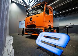 Orangefarbener Mercedes-Benz eActros 600 mit Schade-Logo in einer Halle. Blau leuchtendes E-Symbol im Vordergrund.