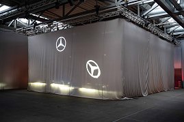 Gro&szlig;es, verh&uuml;lltes Objekt mit Mercedes-Stern-Projektionen in einer Halle vor einer Enth&uuml;llung.