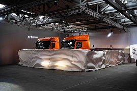Zwei orangefarbene Mercedes-Benz eActros-Lkw mit Schade-Logo, teilweise noch von einer wei&szlig;en Abdeckung umh&uuml;llt.