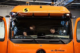 Zwei M&auml;nner pr&uuml;fen das Fahrerhaus eines orangefarbenen Mercedes-Benz eActros von innen.