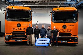 Das Team von Schade Logistic posiert mit 5 Personen vor zwei orangefarbenen Mercedes-Benz eActros-Lkw mit Schade-Logo und leuchtendem E-Symbol.