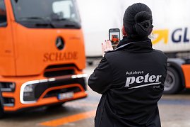Frau im schwarzen Autohaus Peter-Jacke fotografiert einen orangefarbenen Mercedes-Benz eActros mit dem Handy.