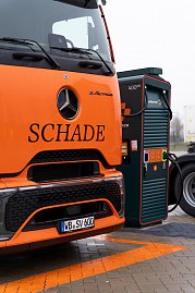 Detailaufnahme eines orangefarbenen Mercedes-Benz eActros mit Schade-Logo an einer gr&uuml;nen Schnelllades&auml;ule mit 400 kW.