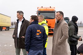 Gruppe von M&auml;nnern in Winterjacken im Gespr&auml;ch. Im Hintergrund ein Schade-Lkw.