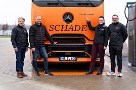 Vier Personen vor einem orangefarbenen Mercedes-Benz eActros-Lkw mit Schade-Logo. Eine Person zeigt auf das eActros-Emblem. Abgebildet von links nach rechts: Frank Hentschel (Verkaufsleiter Trucks, Autohaus Peter GmbH), Bj&ouml;rn Schade (Gesch&auml;ftsf&uuml;hrer Schade Logistics), Christina Dost (Gesch&auml;ftsf&uuml;hrerin Autohaus Peter GmbH), Enrico Dost (Serviceleiter).