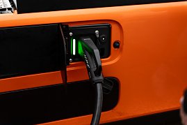 Nahaufnahme eines Ladevorgangs: Ein schwarzes HPC-Ladekabel mit gr&uuml;n leuchtender Anzeige ist an der Seite eines orangefarbenen eActros angeschlossen.