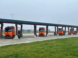Vier eActros 600 Lkw der Firma Schade parken nebeneinander unter einem &uuml;berdachten Ladepark. Ein Fahrer steht jeweils bei den Fahrzeugen.
