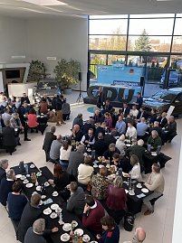 Blick von oben auf viele Vertreter der Wirtschaft, die an schwarzen Tischen mit Kaffee und Geb&auml;ck sitzen. Vorne steht ein Redner, hinten ist eine B&uuml;hne mit CDU-Logo und Bannern zu sehen.