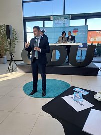 David Gregosz im Anzug spricht vor Publikum in einer Autohaus-Halle. Hinter ihm B&uuml;hne mit CDU-Logo und Podiumsteilnehmern, vorne auf dem Tisch Brosch&uuml;ren und eine Tasse.