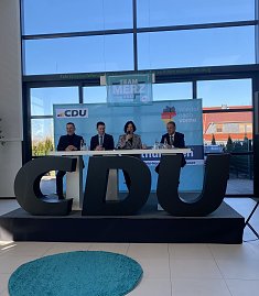 Frontalaufnahme der Podiumsdiskussion mit vier Personen, mittig Colette Boos-John. Vor ihnen gro&szlig;e CDU-Buchstaben, im Hintergrund Team Merz 2025-Plakat.