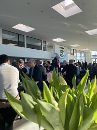 Innenaufnahme des Autohauses mit vielen G&auml;sten, die an schwarzen Tischen sitzen. Im Vordergrund unscharfe Tulpen, im Hintergrund gro&szlig;e Fenster und das Skoda-Logo.